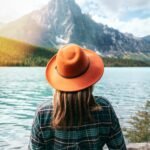 A woman in a fedora enjoys a serene view of a mountain lake in Banff, Canada.
